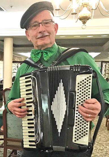 Photo of Tom Brown dressed in green and playing his accordion at a St. Patrick's Day party in 2025